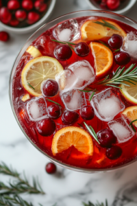 A close-up shot of a glass filled with the Festive Cranberry Pomegranate Punch on the white marble cooktop. The deep red liquid glows under the light, garnished with a floating orange slice and a sprig of rosemary, making it look refreshing and ready to be served.