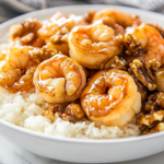 A white serving dish on a white marble cooktop with perfectly coated honey walnut shrimp, garnished with glossy candied walnuts. The dish is served alongside a bowl of fluffy steamed rice, ready to be enjoyed.