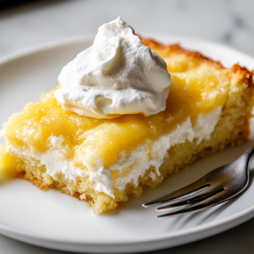A close-up shot of a plate with a warm slice of lemon cream cheese dump cake, served with a dollop of fluffy whipped topping. The layers of lemon filling, soft cake, and creamy cheese are visible, with a fork ready for the first bite.