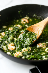 A black skillet on a white marble cooktop with freshly chopped cilantro being stirred into the shrimp and salsa verde mixture. A wooden spoon is mixing everything together, enhancing the dish with fresh herbal notes.