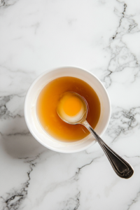 An overhead shot of a mixing bowl with cream cheese, sugar, egg yolk, lemon juice, and vanilla extract being whisked together. The mixture looks smooth, creamy, and rich, ready to be spread onto the pastry.