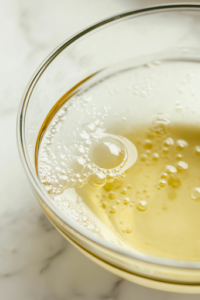 A close-up of another glass mixing bowl on a white marble cooktop, where buttermilk, milk, eggs, and melted butter are being whisked together. The mixture is smooth and well combined, ready to be incorporated into the dry ingredients.