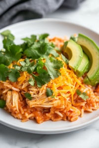 A plated serving of slow cooker chicken and rice in a rustic bowl, garnished with shredded cheese, fresh cilantro, and avocado slices. The dish looks warm, comforting, and full of delicious flavors, ready to be enjoyed.