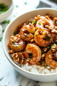 A white serving dish on a white marble cooktop with perfectly coated honey walnut shrimp, garnished with glossy candied walnuts. The dish is served alongside a bowl of fluffy steamed rice, ready to be enjoyed.