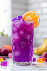 A close-up shot of the finished Potion Punch in a tall glass on the white marble cooktop, garnished with colorful fruit slices and gummy candies. The fizzy, deep purple drink sparkles under the light, looking playful, refreshing, and magical, ready to be enjoyed.