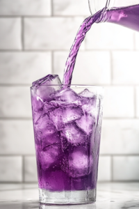A close-up shot of a tall glass filled with ice cubes on the white marble cooktop as Potion Punch is being poured in. The deep purple liquid cascades over the ice, creating a vibrant, fizzy drink with a striking contrast between the dark punch and the clear ice.