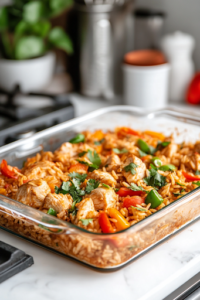 A close-up shot of a glass baking dish on a white marble cooktop, with the freshly baked Chicken Fajita Rice Casserole resting for 5 minutes, allowing the flavors to meld together while the dish slightly cools before serving.