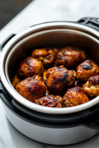 An Instant Pot sits on a white marble cooktop, set to Sauté mode. Chicken thighs or drumsticks sizzle inside, developing a golden brown sear. A pair of tongs is ready to turn the chicken for even browning.