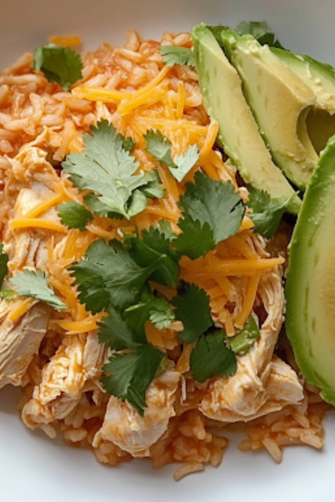 A plated serving of slow cooker chicken and rice in a rustic bowl, garnished with shredded cheese, fresh cilantro, and avocado slices. The dish looks warm, comforting, and full of delicious flavors, ready to be enjoyed.