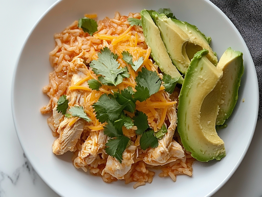 A plated serving of slow cooker chicken and rice in a rustic bowl, garnished with shredded cheese, fresh cilantro, and avocado slices. The dish looks warm, comforting, and full of delicious flavors, ready to be enjoyed.
