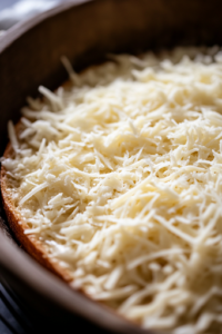 A slice of crispy garlic bread rests on a wooden cutting board. A generous layer of the creamy chicken mixture is being spread evenly with a spoon, covering the surface while leaving a slight edge for balance.