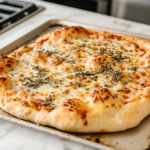 A close-up of a freshly baked golden-brown pizza on a baking sheet over the white marble cooktop. The crust is crisp and bubbly, with melted cheese and toppings glistening, ready to be sliced and served.