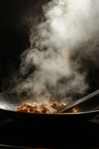 Action shot of a wok on high heat, with marinated chicken sizzling in oil, turning golden brown. Steam rises as the chicken is being stir-fried with a spatula