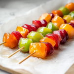 A close-up shot of a completed Candied Fruit Skewer being lifted from the parchment paper on the white marble cooktop. The glossy sugar shell glistens under the light, cracking slightly as it's ready to be enjoyed, revealing the fresh, juicy fruit inside.