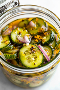 The cooled pickle mixture is being carefully transferred into sterilized glass jars on the white marble cooktop. The vibrant green cucumbers and soft onions float in the golden turmeric-infused liquid, creating a bright and appetizing contrast.