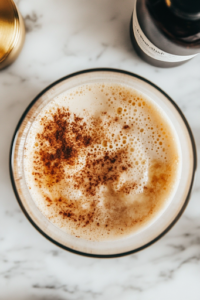 A close-up of a glass mixing bowl on a white marble cooktop, filled with eggs, half-and-half, vanilla extract, cinnamon, brown sugar, and a pinch of salt. A whisk is blending the ingredients together into a smooth, golden mixture, ready to coat the Hawaiian rolls.