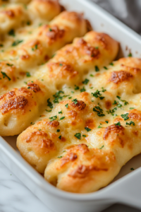 A close-up shot of the golden brown, bubbly cheesy breadsticks fresh out of the oven in the baking dish over the white marble cooktop. The cheese is perfectly melted, with crispy edges.