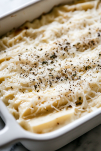 A close-up shot of the dough in the baking dish over the white marble cooktop, now brushed with melted butter. Shredded mozzarella, grated parmesan, garlic salt, and dried oregano are sprinkled on top, creating a rich, cheesy layer.