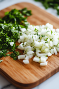A close-up shot of finely diced onion and freshly chopped cilantro on a wooden cutting board over the white marble cooktop. The bright colors contrast beautifully before being added to the bowl.