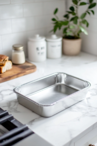A greased 9x5-inch loaf pan sits on a white marble cooktop, ready for baking. The oven in the background is preheating to 350°F (175°C).