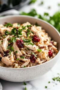 A steaming bowl of Instant Pot Chicken and Wild Rice, garnished with freshly chopped parsley. The dish is colorful, hearty, and ready to serve, with shredded chicken, plump cranberries, and fluffy rice perfectly combined.