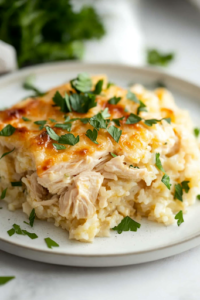 A serving of baked chicken and rice casserole on a white plate, garnished with freshly chopped parsley. The dish looks warm, comforting, and ready to be enjoyed.