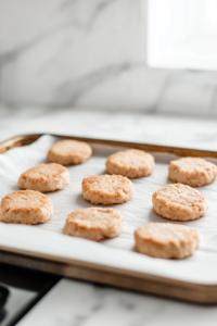 Close-up of ten evenly shaped, slightly flattened crab cakes resting on a parchment-lined tray over the white marble cooktop, ready for coating.