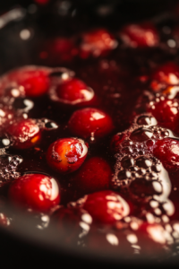 Close-up of the simmering kompot, with the fruit floating in the deepening, richly colored liquid. The heat creates tiny bubbles around the edges as the flavors infuse together.