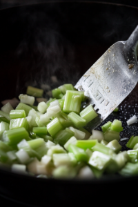 Overhead shot of a wok where crisp celery and white onions are being stir-fried in hot oil. The vegetables maintain their vibrant color and crisp texture as a spatula tosses them.