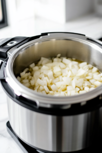 Minced garlic being stirred into the softened onions inside the Instant Pot over the white marble cooktop. A wooden spoon is in motion.