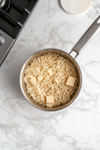 A top-down view of uncooked ramen bricks placed in a medium saucepan with boiling water on a white marble countertop. The noodles are ready to be cooked, with a strainer nearby for draining. The background is minimal and clean, with the focus on the noodles in the pot, reflecting the simplicity of the cooking process.