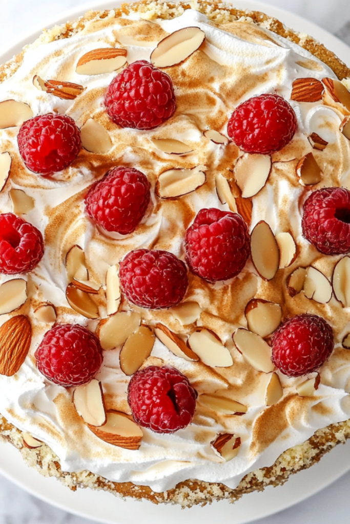 A top-down view of the completed Heaven Cake, beautifully garnished with fresh raspberries and a dusting of powdered sugar, placed on a white marble countertop. The layers are visible, showcasing the light whipped cream filling and golden meringue crust. The simple and clean background emphasizes the cake's delicate and inviting appearance, ready to be served chilled.