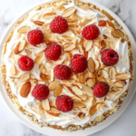 A top-down view of the completed Heaven Cake, beautifully garnished with fresh raspberries and a dusting of powdered sugar, placed on a white marble countertop. The layers are visible, showcasing the light whipped cream filling and golden meringue crust. The simple and clean background emphasizes the cake's delicate and inviting appearance, ready to be served chilled.