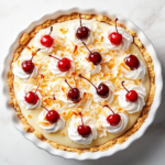 Top-down image of the finished tropical coconut pineapple cream pie, beautifully garnished with swirls of whipped cream and bright red maraschino cherries on top. The golden crust holds layers of coconut custard and pineapple topping. The pie is presented on a clean white marble surface, capturing the vibrant, creamy, and tropical essence of the dessert.