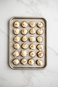 Top-down image of golden brown stuffed mushrooms freshly baked and arranged on a silver baking tray. The creamy filling is bubbling and slightly crisped on top. The tray rests on a clean white marble surface, capturing the final step before serving this warm and savory mushroom-based dish to guests.