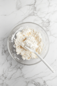 A spatula gently folds whipped topping into the cream cheese mixture, creating an airy and creamy consistency. This careful mixing technique helps maintain a light and fluffy texture for the dessert.