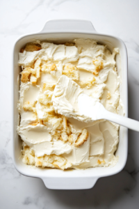 A 9x13-inch dish is being filled with evenly torn pieces of soft angel food cake. The light and spongy cake layer will absorb the creamy mixture, creating a delicious base for the dessert.