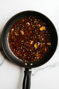 Mushrooms are simmering slowly in the rich oyster sauce blend inside a black skillet on a white marble countertop. The sauce thickens while the mushrooms become fully tender and soaked with flavor. The final stage of cooking ensures that the mushrooms are juicy, well-seasoned, and ready to serve warm.