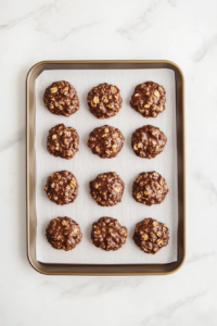 A top-down view of several no-bake chocolate oatmeal cookies placed neatly on a tray lined with parchment paper. The cookies are round, dark chocolate brown with visible oats, and slightly glossy from the peanut butter and cocoa mixture. They rest on a white marble countertop, cooled and ready to serve or store.