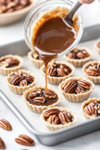 A ladle is being used to carefully spoon the sweet egg-based filling into the mini pie shells, covering the pecans and filling each shell about three-quarters full. The filling includes eggs, sugar, corn syrups, butter, vanilla, and salt. This step ensures each bite has the perfect mix of creamy filling and crunchy pecans.