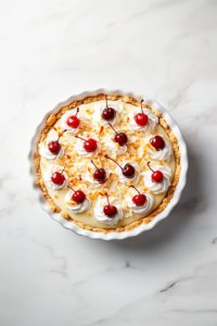Top-down image of the finished tropical coconut pineapple cream pie, beautifully garnished with swirls of whipped cream and bright red maraschino cherries on top. The golden crust holds layers of coconut custard and pineapple topping. The pie is presented on a clean white marble surface, capturing the vibrant, creamy, and tropical essence of the dessert.